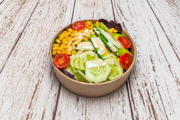 A wonderful salad with fresh cucumber, tomatoes, and avocado inside a cardboard container