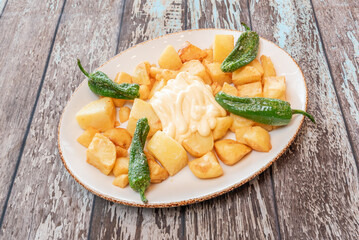 A tapa of chips with sauce and fried peppers on a wooden table