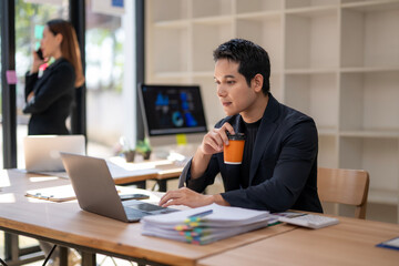A man is sitting at a desk with a laptop and a cup of coffee