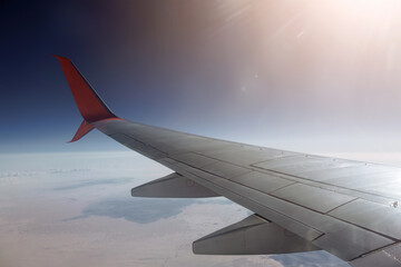 Obraz premium Airplane wing soaring over vast desert landscape, illuminated by the soft light of dawn. The curvature of the wing and the expanse of the scenery create a sense of limitless travel and exploration.
