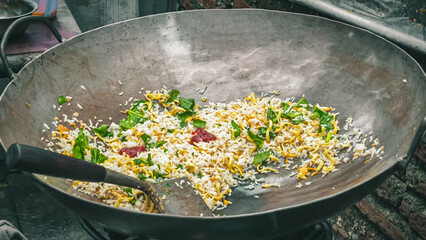 Close-up of fried rice with green leafy vegetables in a wok on a stove