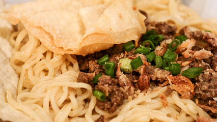 Close-up of savory noodle dish with crispy toppings and vibrant scallions