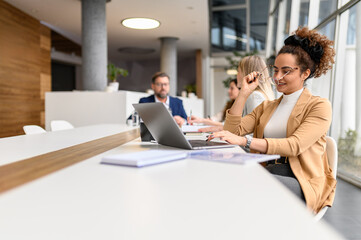 Businesswoman wearing eyeglasses while analyzing data over laptop in office with coworkers in the...