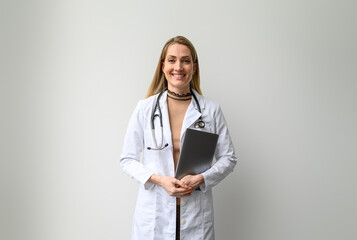 Portrait of confident female doctor in lab coat holding laptop and standing against white background