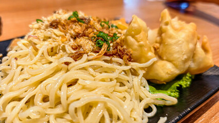 Delicious Asian noodles with crispy fried wontons served on a black plate