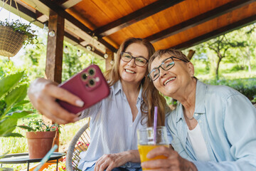 Two mature women friends mother and daughter taking selfie on smartphone on sunny terrace of country house