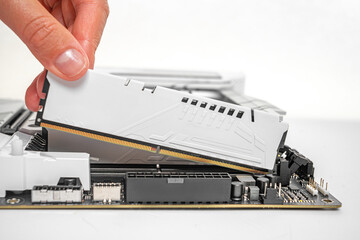 A person is carefully inserting a white DDR RAM module into a motherboard slot during a desktop...