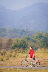 A Handsome young man in a red shirt and black sports shorts is happily riding a white bicycle in...