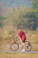A Handsome young man in a red shirt and black sports shorts is happily riding a white bicycle in...