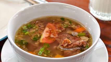 A steaming and delicious bowl of beef rib soup, complete with fresh vegetables, fragrant herbs, and juicy tomato slices. This hearty dish offers comfort and a delightful culinary experience