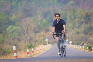 Handsome young man in a blue shirt and black sports shorts is happily riding a bronze and blue...