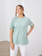Woman with brown hair wearing mint green short-sleeve shirt and white pants, posing with hand on...