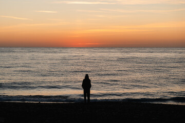 Person stands by the shore, watching the serene sunrise over Cirali Beach, Turkey, in the morning.