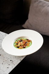 A gourmet dish with green puree, crispy bacon, fried onions, and dark sauce, elegantly plated on a...