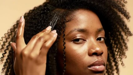 Woman of color gently applies a styling product with her fingers to her curly hair, defining edges, showcasing care for textured hair, promoting beauty and self-care