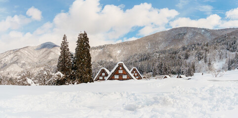 A panoramic view of three traditional gassho-zukuri houses in Shirakawa-go, Japan, surrounded by snow-covered fields and distant mountains in the background. UNESCO World Heritage 