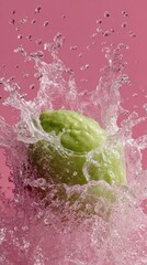 A vibrant splash of smoothie explodes upward in slow-motion, creating intricate water droplets. The scene features a green fruit at the center amidst a playful pink backdrop