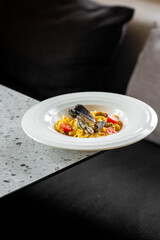 Seafood pasta with mussels and cherry tomatoes, served on a terrazzo table against a dark background. Elegant presentation highlights vibrant colors and textures.