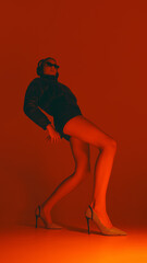 Obraz premium Young woman standing in dynamic pose, showing contemporary fashion look with sunglasses and striking footwear against vibrant red background in neon light. Concept of fashion, style, youth culture
