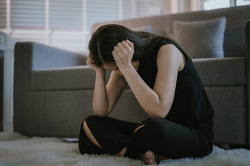 Depressed and unhappy Asian woman sits with anxiety on the sofa in her living room at home.