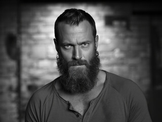 Obraz premium A dramatic black and white portrait photograph of a rugged man with a very large, well-groomed, dark brown beard and piercing blue eyes