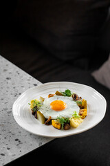 A gourmet dish with a sunny-side-up egg, garnished with herbs, accompanied by corn, potatoes, and mushrooms, served on a white plate over a speckled countertop.