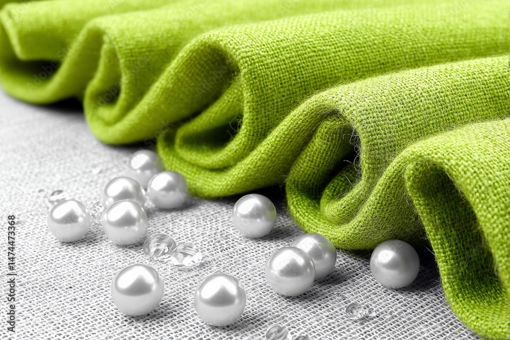 Poster delicate green fabric rolled up with scattered pearls on a textured surface
