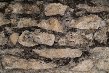 Close Up Texture Of An Ancient, Rough Wall Made Of Unevenly Shaped Natural Stones And Weathered Mortar. Historical Masonry Background Found In Old Buildings.