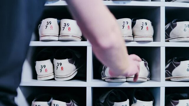 Organized rows of bowling shoes as person selects a pair by hand indoors