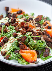 Fresh salmon salad with arugula, crispy croutons, sunflower seeds and creamy green sauce served on a white plate, offering a healthy and delicious meal