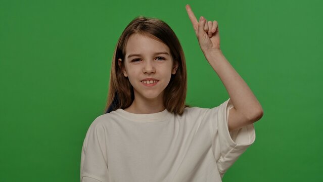 Teenage girl posing at camera pointing finger up, positive expression, isolated on chroma key green screen studio background mockup.