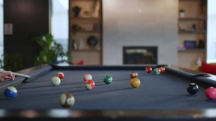 Colorful billiard balls are scattered across a pool table in a modern lounge. A cozy atmosphere surrounds the table as friends enjoy their time during a leisurely afternoon.