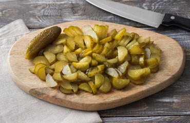Salty cucumber slices on a wooden board on wooden table, rustic style, top view