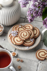 Two colored pinwheal homemade cookies with vanilla and chocolate flavor in shape of spiral on gray tile background with tea and flowers. Cozy breakfast