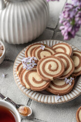 Two colored pinwheal homemade cookies with vanilla and chocolate flavor in a shape of spiral on gray tile background with tea and flowers close up