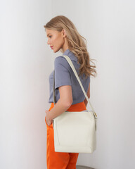 Blonde Woman in Stylish Outfit Poses With Handbag in Modern Indoor Setting