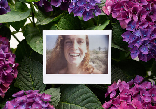 Blank instant photo is placed among vibrant purple flowers.