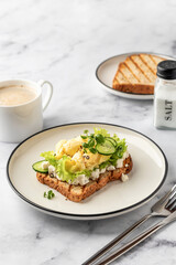 Scrambled eggs on grilled toast with salad leaves, cheese and micro greens on plate on white marble background. Delicious breakfast, brunch, snack