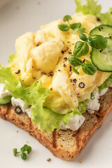 Scrambled eggs on grilled toast with salad leaves, cheese and micro greens on plate close up. Delicious healthy breakfast
