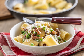 Typical Italian pasta Calamarata with bacon, fresh peas and parmesan cheese