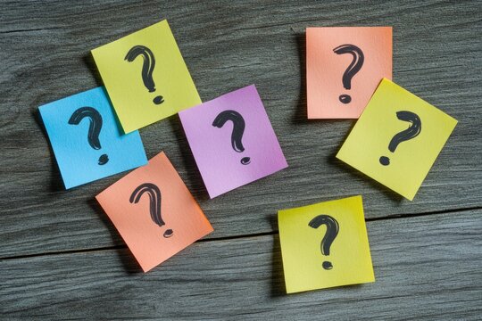 Assorted colorful sticky notes with question marks scattered on a wooden surface