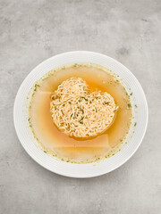 Instant heart shape noodles floating in broth on white plate, prague, czechia copy space Valentines Mothers Dads day
