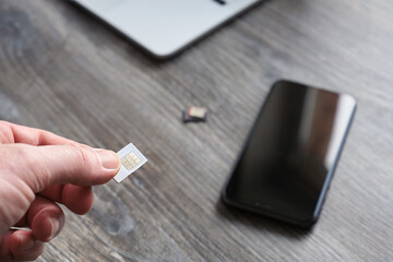 Male hand holding a SIM card for a smartphone, against the background of a wooden table, phone and...