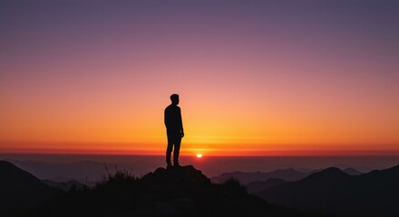 Silhouetted figure atop a mountain at sunrise.