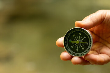 Hand holding a compass in nature with green background. Close-up. Copy space. © Marinela