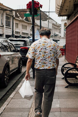Obraz premium Man walking on city sidewalk carrying plastic bag, rear view