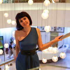 A graceful woman in a stunning blue off-shoulder dress strolls elegantly towards restaurant for...