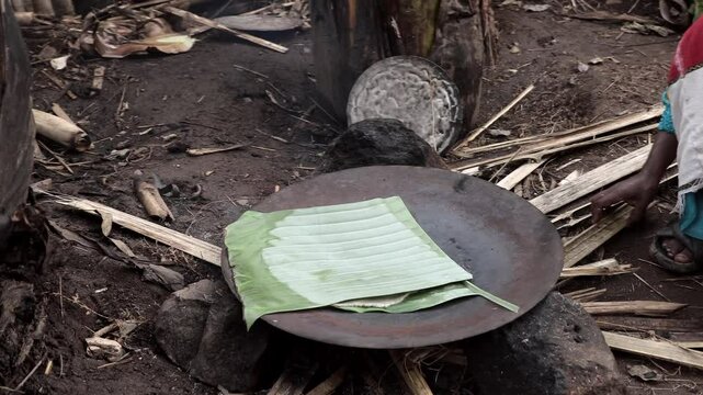 A woman cooks in banana leaves over an open fire at a village in Southern Ethiopia near Konso.