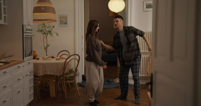 Guy and a girl in pajamas dance an impromptu dance with elements of a waltz during a fun and romantic vacation in a cozy apartment at home