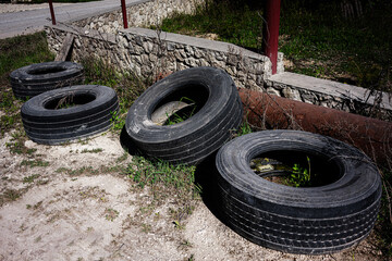 Four discarded tires near a stone wall and grass area in sunlight
